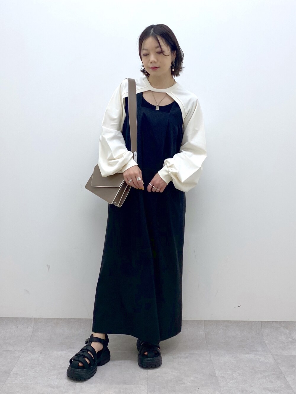 ブラック系のジャンパースカート、ホワイト系のTシャツ/カットソー、ブラウン系のショルダーバッグを着用したレディースの春コーディネートの1枚目の写真