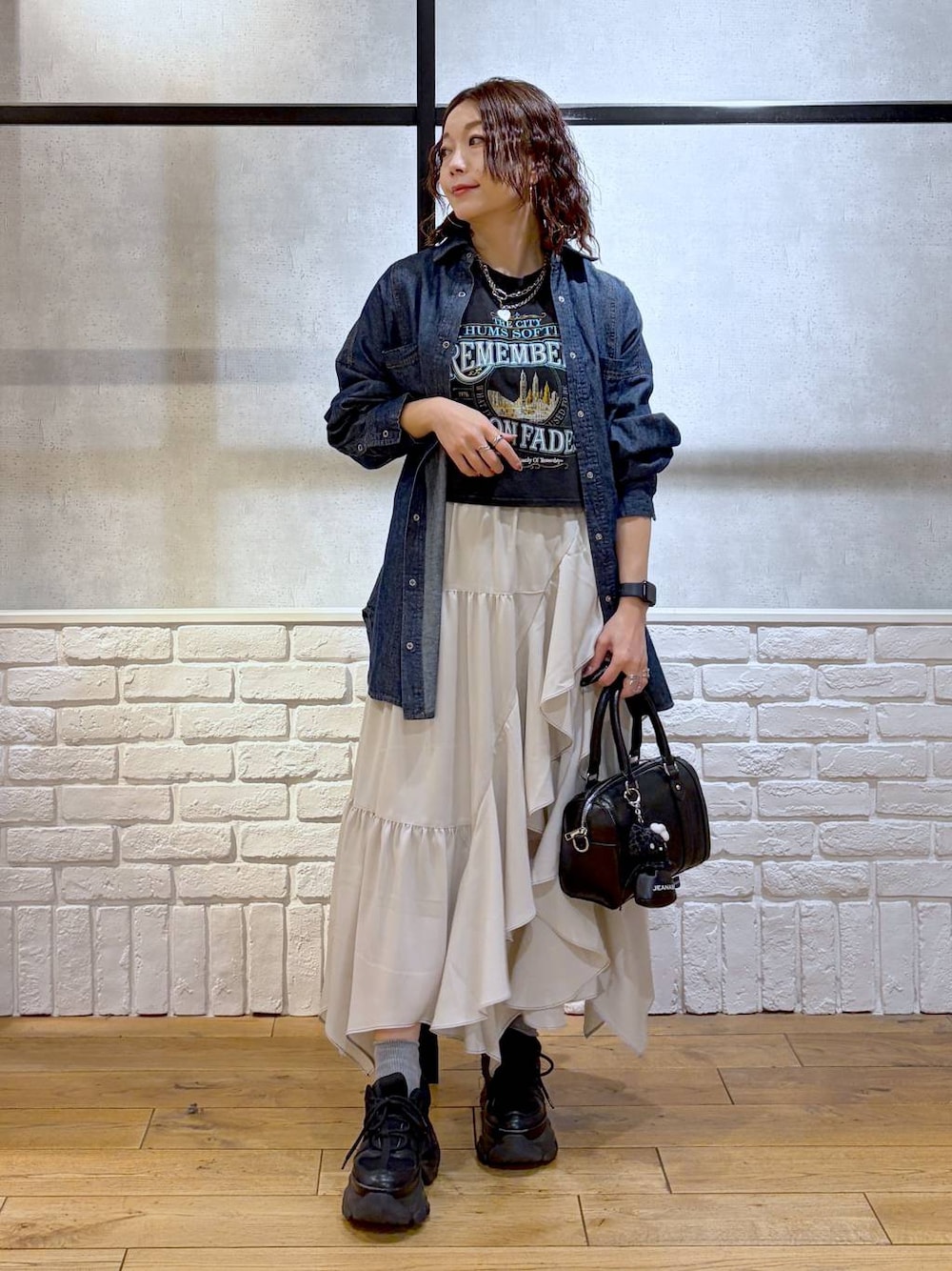 ブラック系のスニーカー、ベージュ系のスカート、ブラック系のボストンバッグを着用したレディースの春コーディネートの1枚目の写真