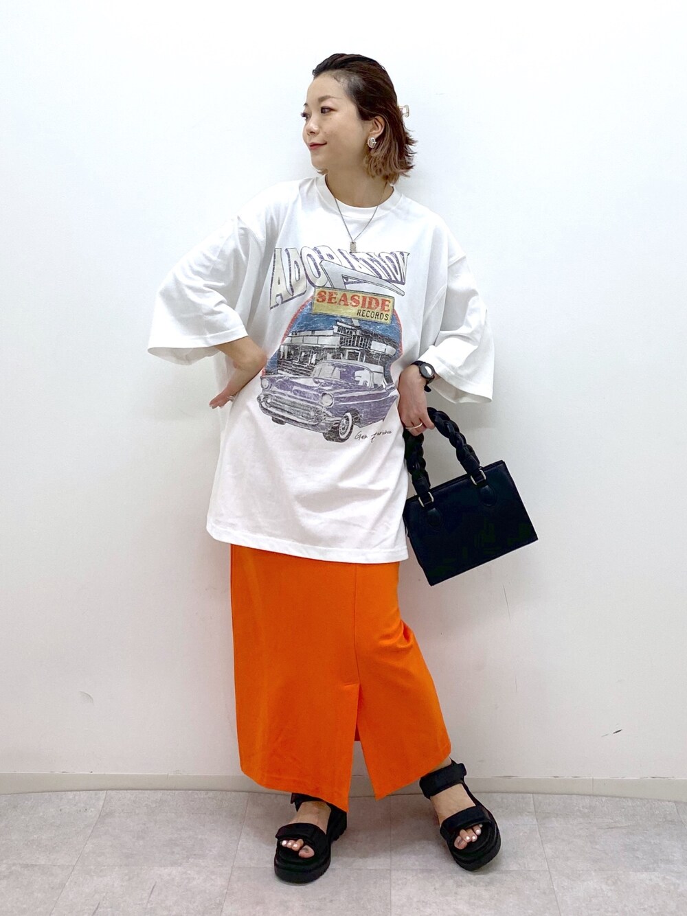 ホワイト系のTシャツ/カットソー、オレンジ系のスカート、ブラック系のショルダーバッグを着用したレディースの夏コーディネートの1枚目の写真