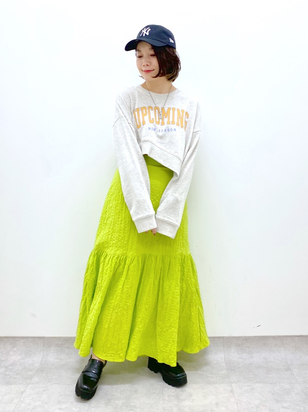 イエロー系のスカート、ベージュ系のトップス、ブラック系のローファーを着用したレディースの春コーディネートの1枚目の写真