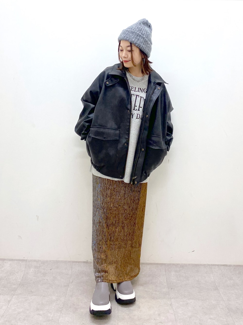 グレー系のニット/セーター、ブラック系のブルゾン、ゴールド系のスカートを着用したレディースの秋コーディネートの1枚目の写真