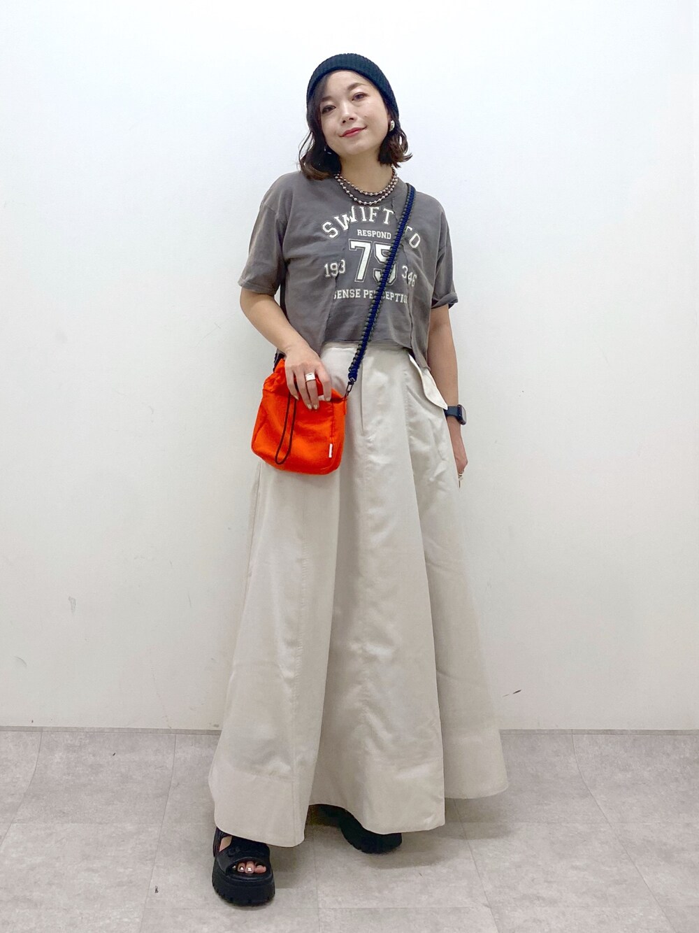 ブラック系のTシャツ/カットソー、オレンジ系のショルダーバッグ、ベージュ系のスカートを着用したレディースの夏コーディネートの1枚目の写真