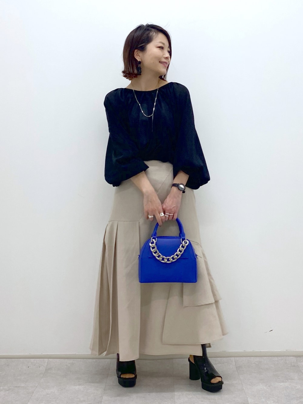 ブラック系のシャツ/ブラウス、ブルー系のショルダーバッグ、ベージュ系のスカートを着用したレディースの春コーディネートの1枚目の写真