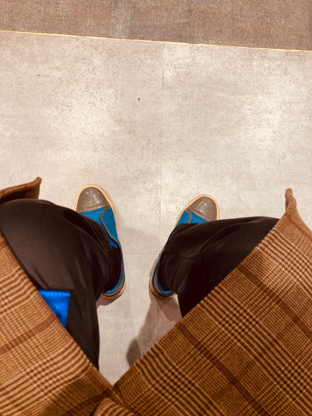 ブルー系のシューズ、ブラウン系のトレンチコート、ブラック系のチノパンツを着用したメンズの冬コーディネートの1枚目の写真