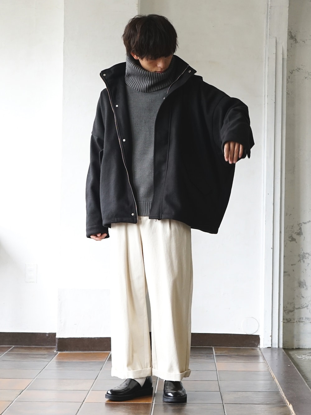 ブラック系のマウンテンパーカー、グレー系のニット/セーター、ホワイト系のデニムパンツを着用したメンズの冬コーディネートの1枚目の写真