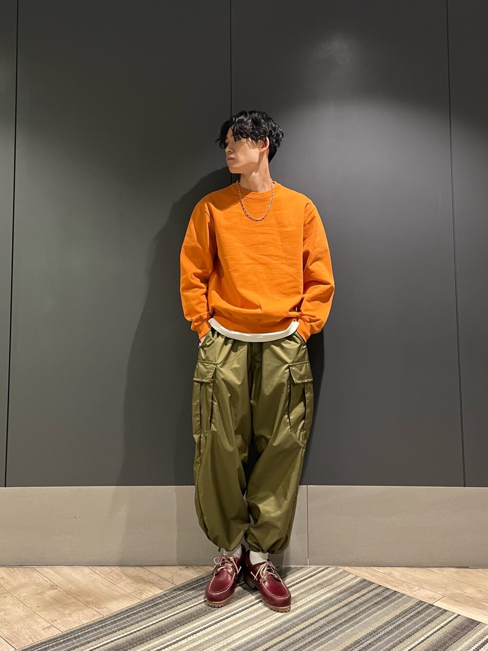 オレンジ系のスウェット、ブラウン系のモカシン/デッキシューズ、シルバー系のネックレスを着用したメンズの春コーディネートの1枚目の写真
