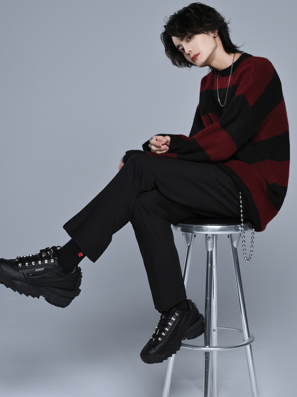 レッド系のニット/セーター、ブラック系のスラックス、ブラック系のスニーカーを着用したメンズの秋コーディネートの1枚目の写真