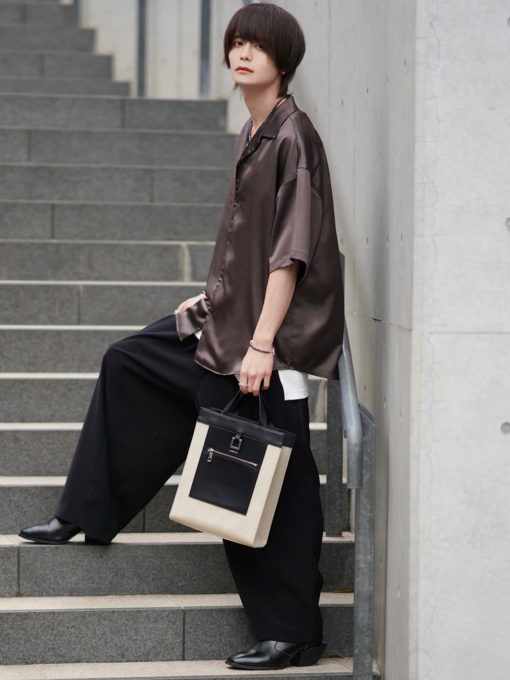 ブラック系のスラックス、ブラック系のブーツ、ベージュ系のトートバッグを着用したメンズの春コーディネートの1枚目の写真