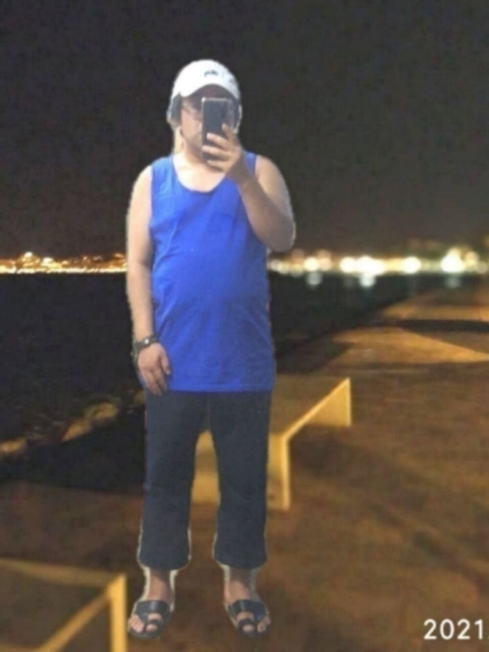 ブルー系のタンクトップ、ブルー系のチノパンツ、ホワイト系のキャップを着用したメンズの夏コーディネートの1枚目の写真