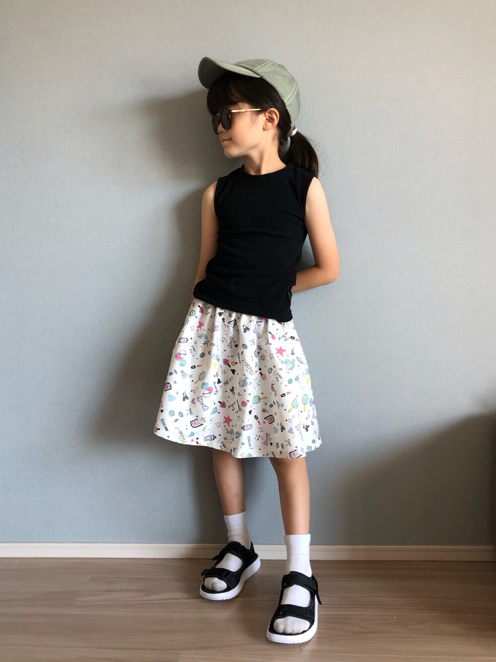 ブラック系のタンクトップ、ホワイト系のスカート、ブラック系のサンダルを着用したキッズの夏コーディネートの1枚目の写真