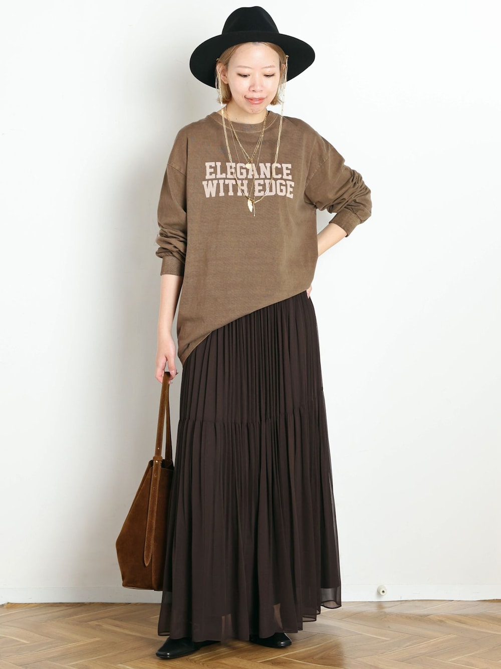 ブラウン系のスカート、ベージュ系のTシャツ/カットソー、ブラック系のブーツを着用したレディースの秋コーディネートの1枚目の写真