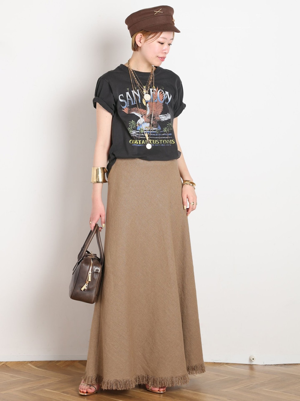イエロー系のスカート、ブラック系のTシャツ/カットソー、ゴールド系のサンダルを着用したレディースの春コーディネートの1枚目の写真