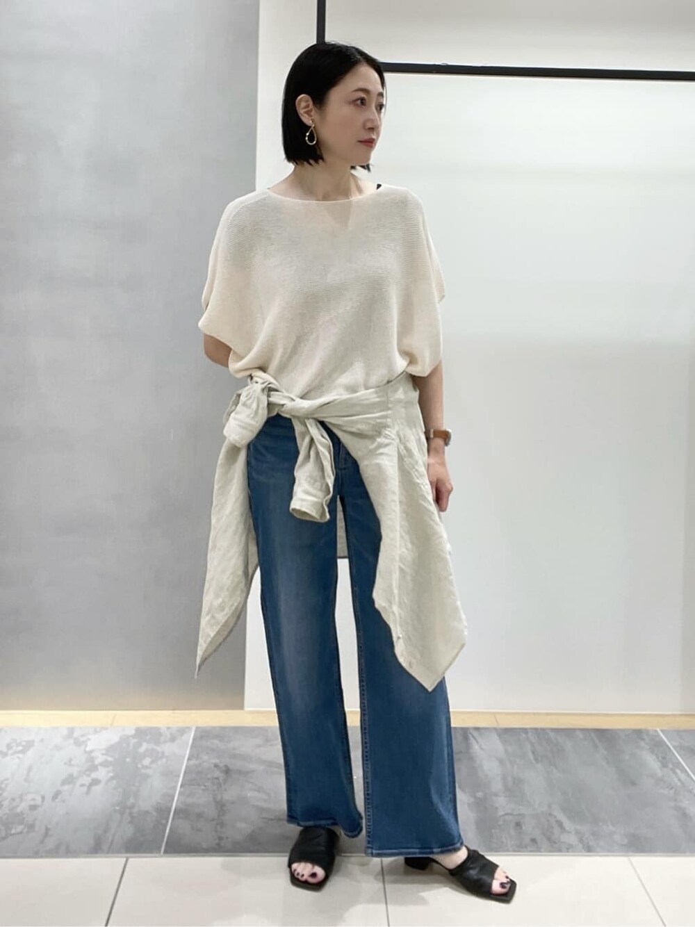 グレー系のデニムパンツ、ベージュ系のシャツ/ブラウス、ベージュ系のニット/セーターを着用したレディースの春コーディネートの1枚目の写真