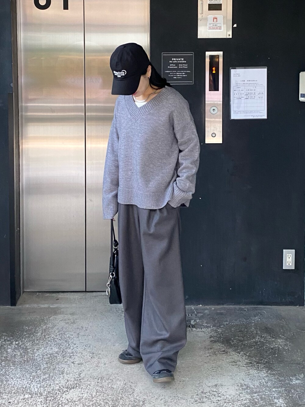グレー系のニット/セーター、グレー系のスラックス、ブラック系のショルダーバッグを着用したレディースの秋コーディネートの1枚目の写真