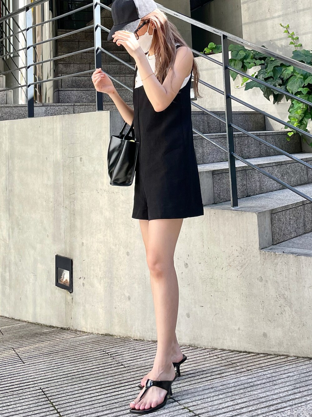 ブラック系のハンドバッグ、ブラック系のオールインワン・サロペット、ブラック系のサンダルを着用したレディースの夏コーディネートの1枚目の写真