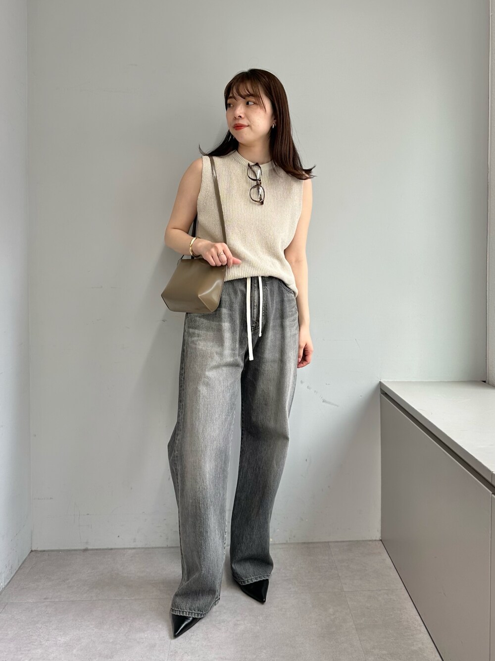 グレー系のデニムパンツ、ベージュ系のニット/セーター、ブラウン系のショルダーバッグを着用したレディースの春コーディネートの1枚目の写真