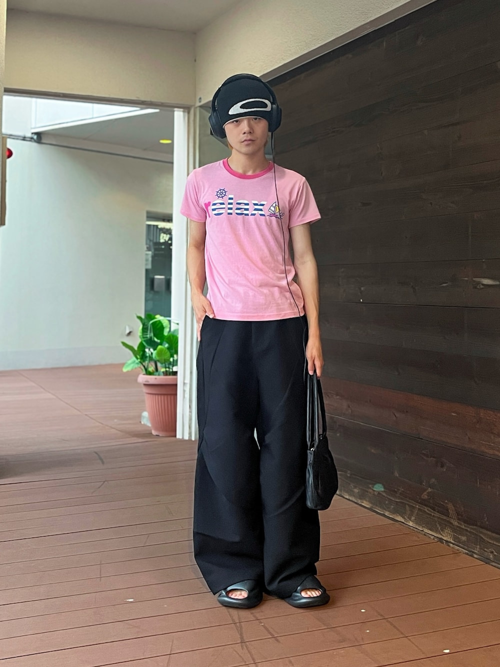 ピンク系のTシャツ/カットソー、ブラック系のスラックス、ブラック系のハンドバッグを着用したメンズの夏コーディネートの1枚目の写真