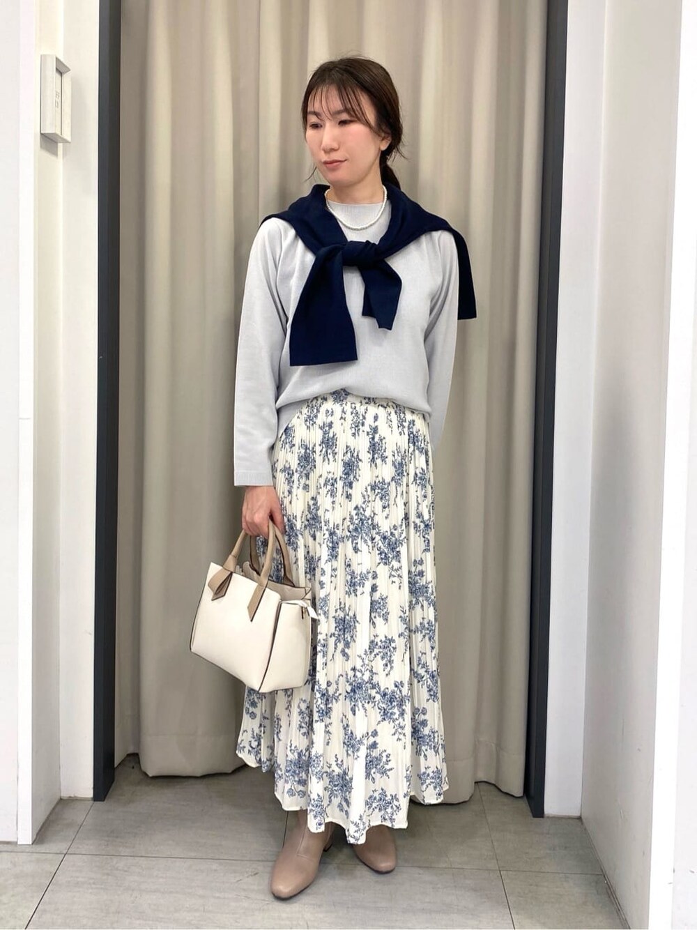 グレー系のニット/セーター、ブルー系のカーディガン/ボレロ、ホワイト系のスカートを着用したレディースの冬コーディネートの1枚目の写真