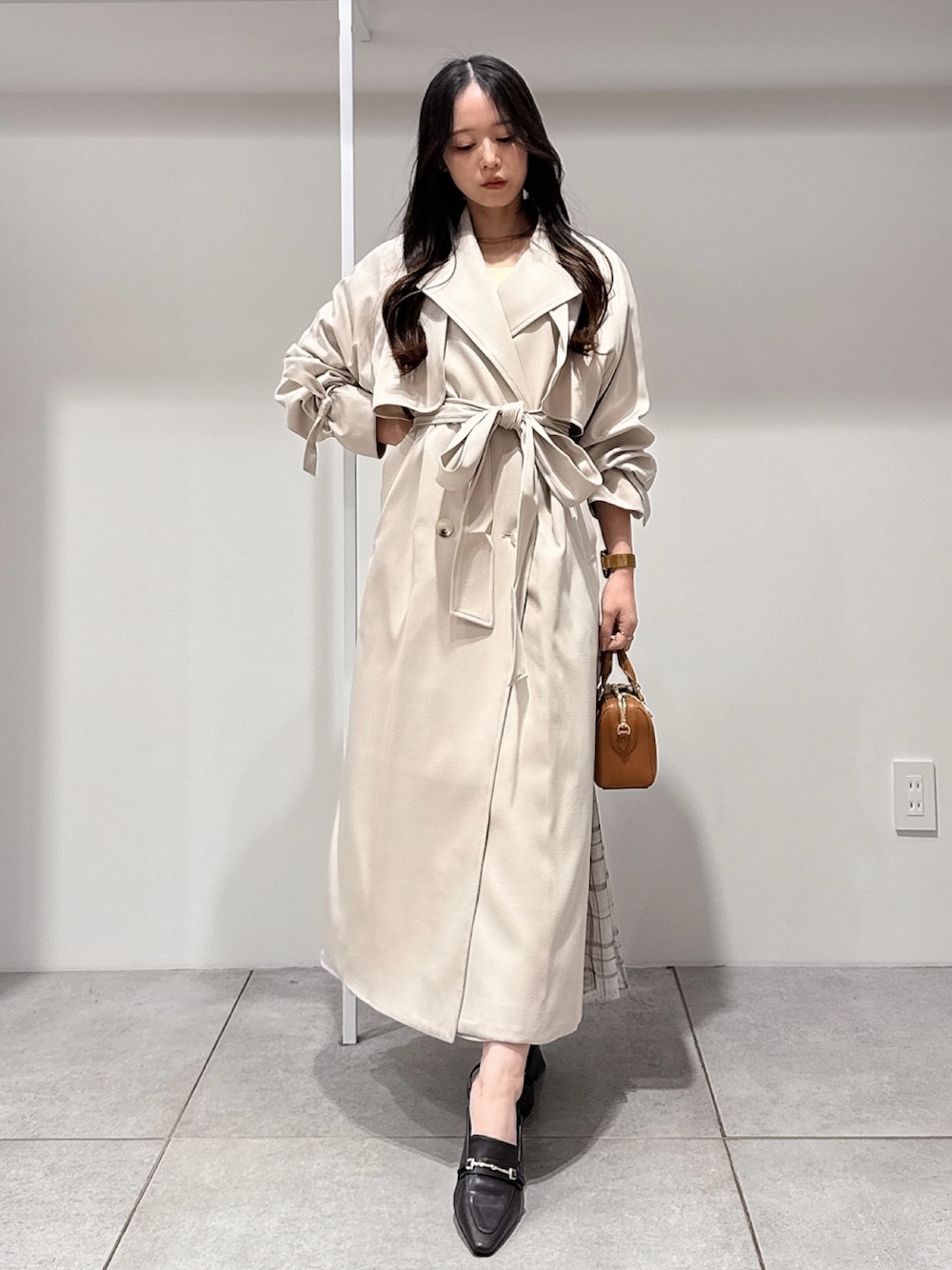 ベージュ系のトレンチコート、ブラウン系のハンドバッグ、ブラウン系のパンプスを着用したレディースの冬コーディネートの1枚目の写真