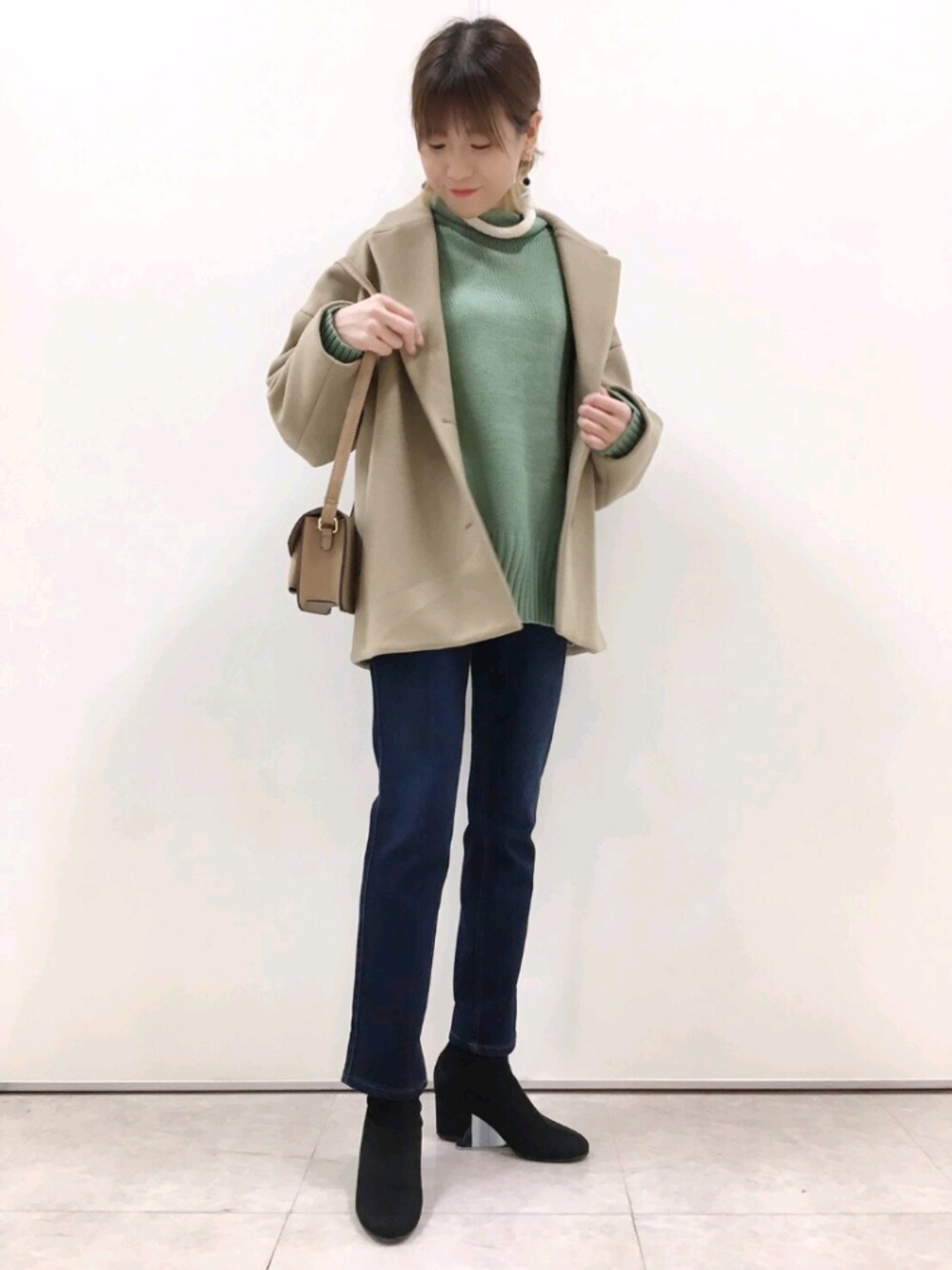 グリーン系のニット/セーター、ベージュ系のチェスターコート、ブルー系のパンツを着用したレディースの冬コーディネートの1枚目の写真