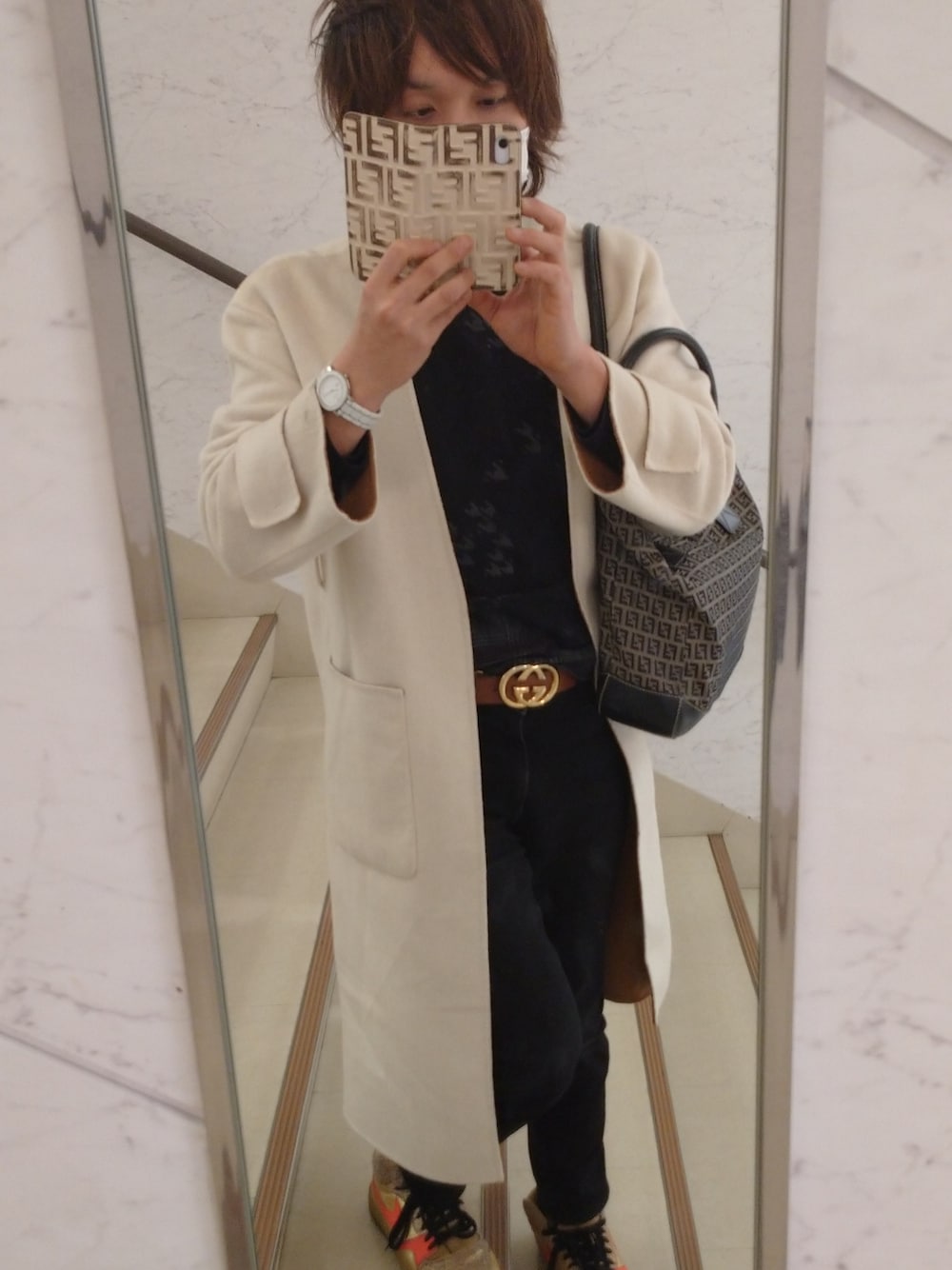 ゴールド系のスニーカー、ブラック系のTシャツ/カットソー、ホワイト系のノーカラーコートを着用したメンズの冬コーディネートの2枚目の写真