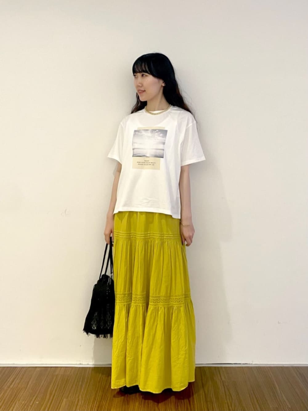 ホワイト系のTシャツ/カットソー、ブラック系のトートバッグ、イエロー系のスカートを着用したレディースの夏コーディネートの1枚目の写真