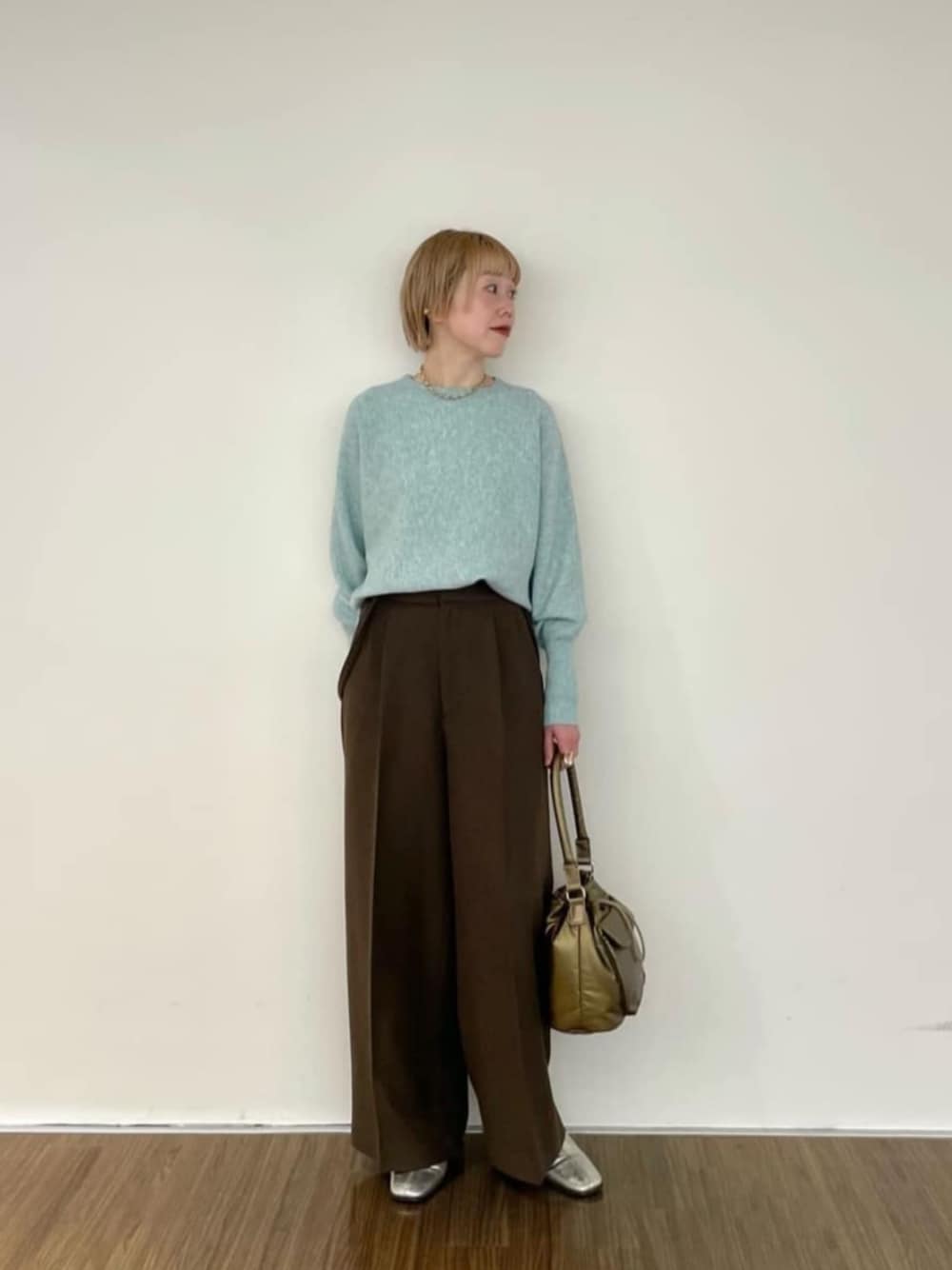 グリーン系のニット/セーター、ブラウン系のその他パンツ、ゴールド系のハンドバッグを着用したレディースの冬コーディネートの1枚目の写真
