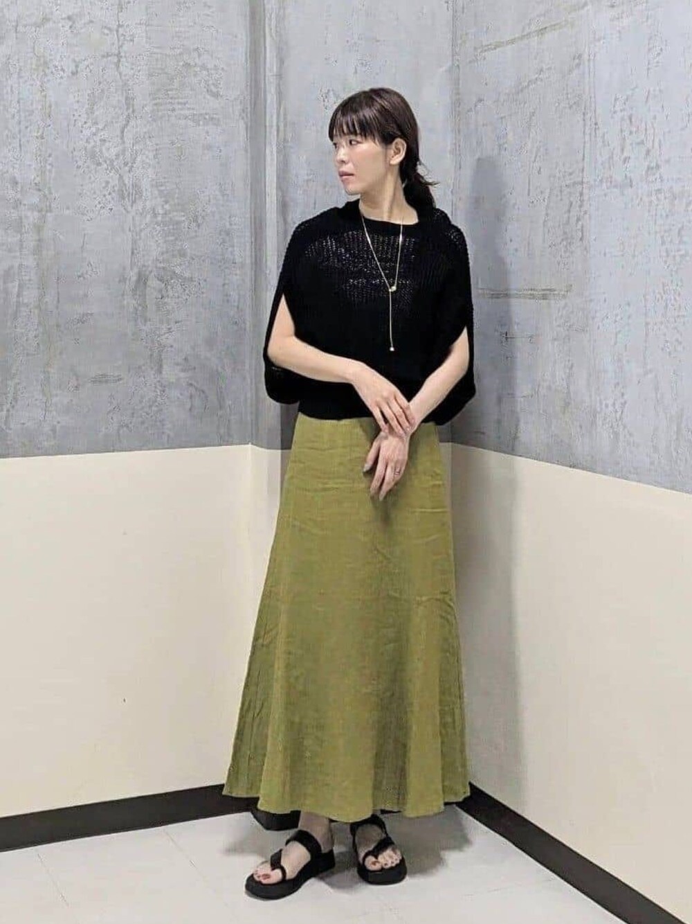 ブラック系のニット/セーター、ブラック系のサンダル、グリーン系のスカートを着用したレディースの夏コーディネートの1枚目の写真