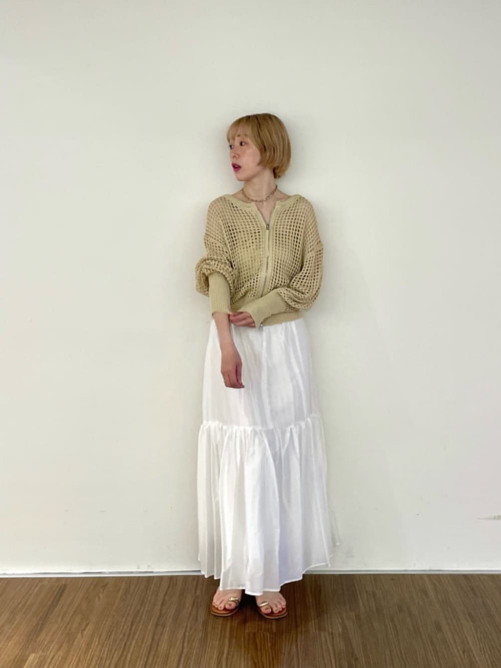 ホワイト系のスカート、ゴールド系のチューブトップ、ベージュ系のカーディガン/ボレロを着用したレディースの春コーディネートの1枚目の写真