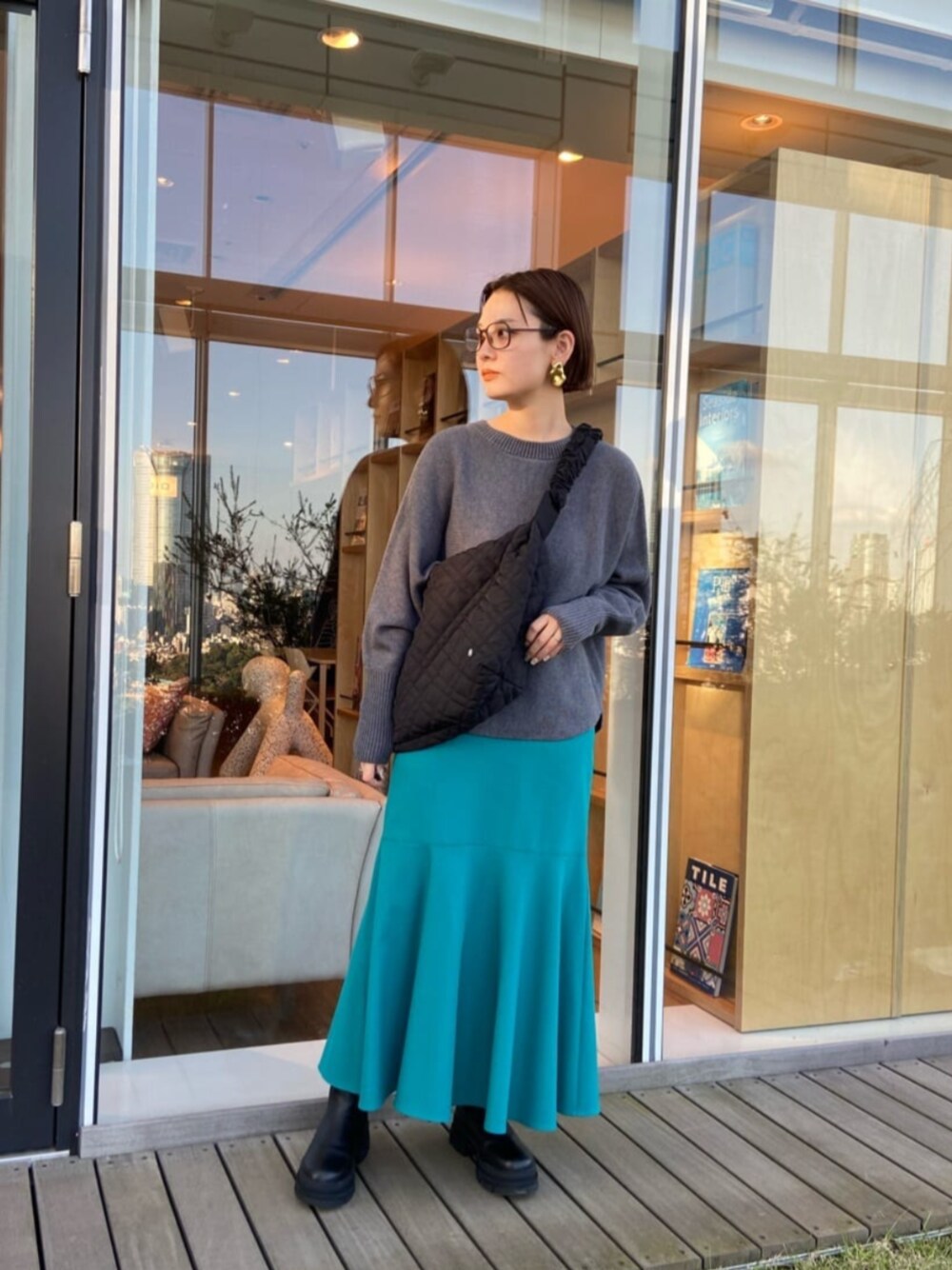 ブルー系のスカート、グレー系のニット/セーター、ブラック系のショルダーバッグを着用したレディースの秋コーディネートの1枚目の写真