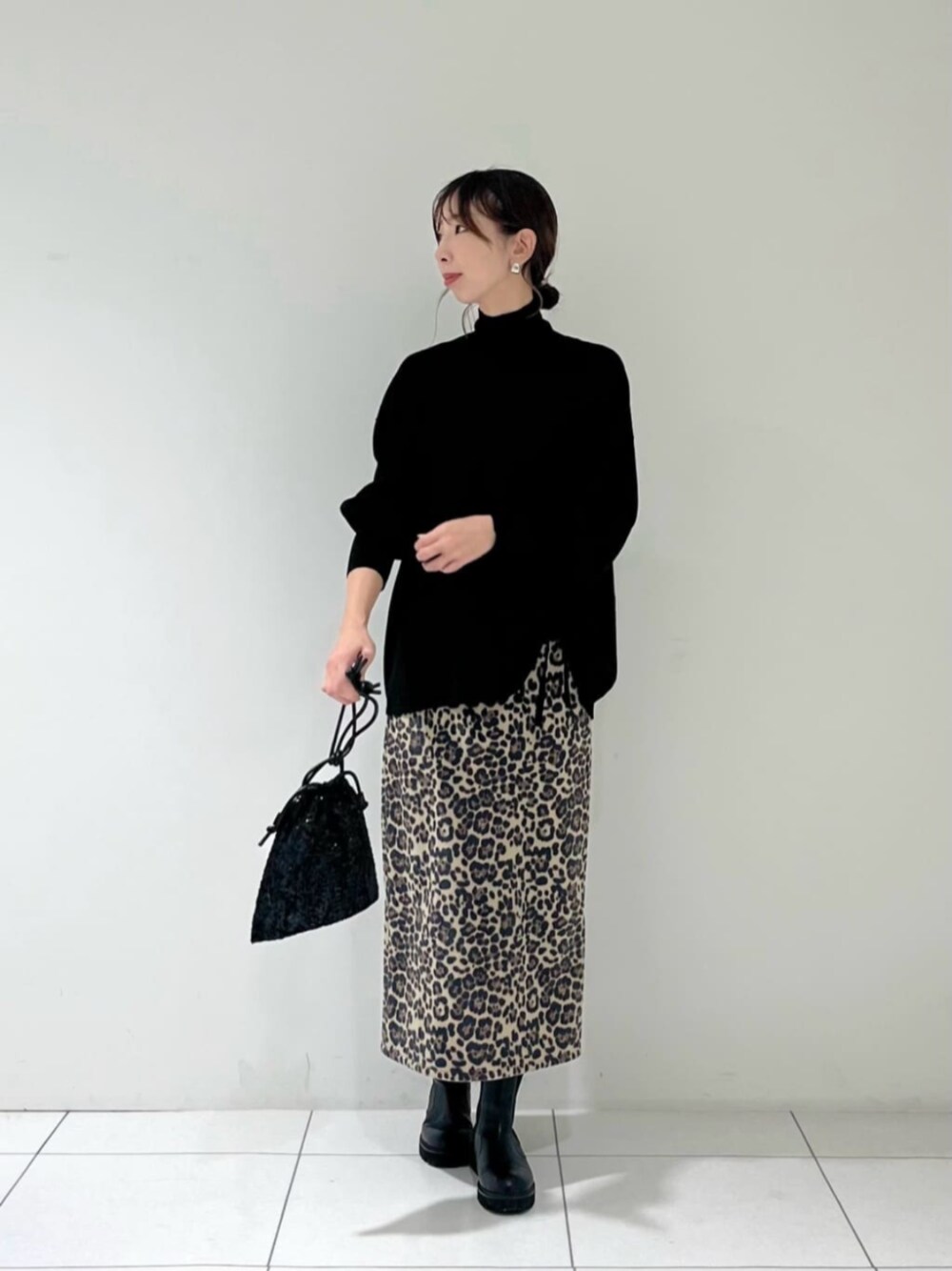 ブラック系のショルダーバッグ、ブラック系のニット/セーター、ブラウン系のスカートを着用したレディースの秋コーディネートの1枚目の写真