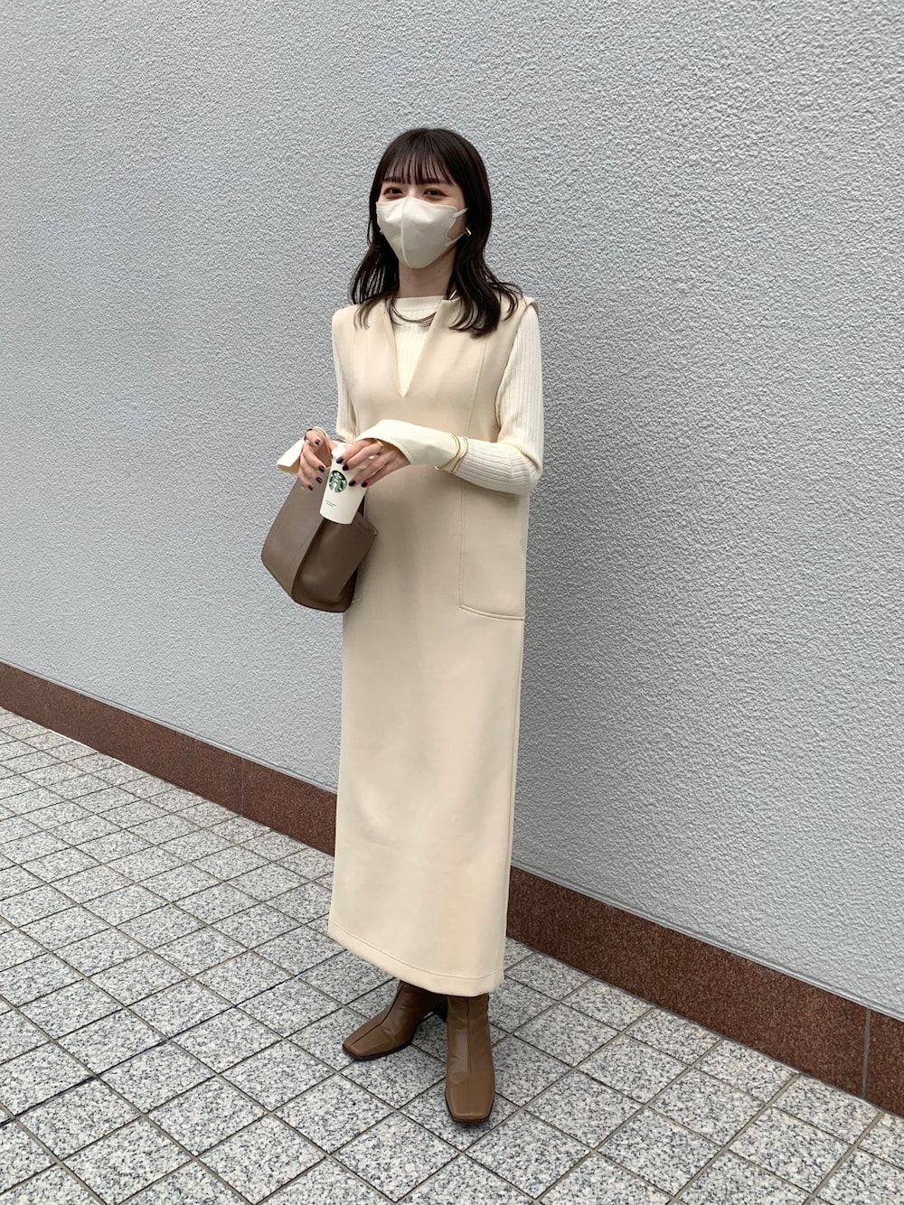 ベージュ系のワンピース、ホワイト系のニット/セーター、ブラウン系のブーツを着用したレディースの秋コーディネートの2枚目の写真