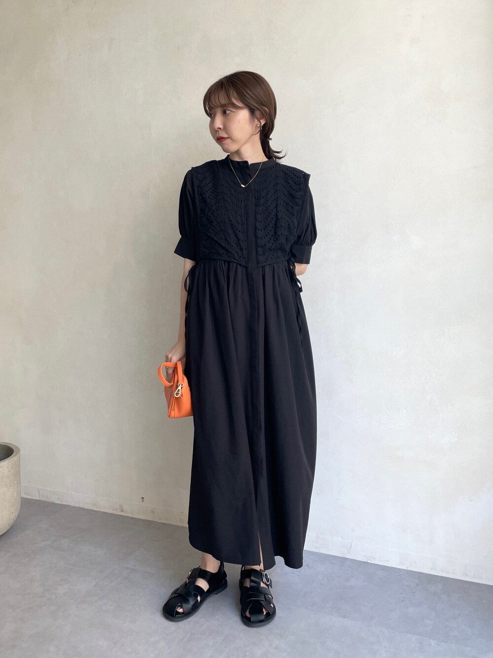 ブラック系のワンピース、オレンジ系のショルダーバッグ、ブラック系のサンダルを着用したレディースの夏コーディネートの1枚目の写真