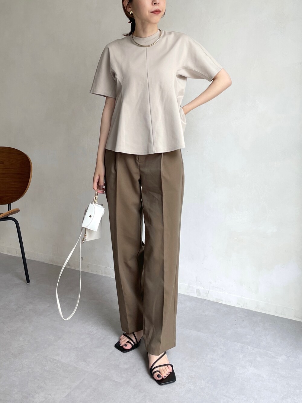 ベージュ系のTシャツ/カットソー、ブラウン系のスラックス、ホワイト系のショルダーバッグを着用したレディースの夏コーディネートの2枚目の写真