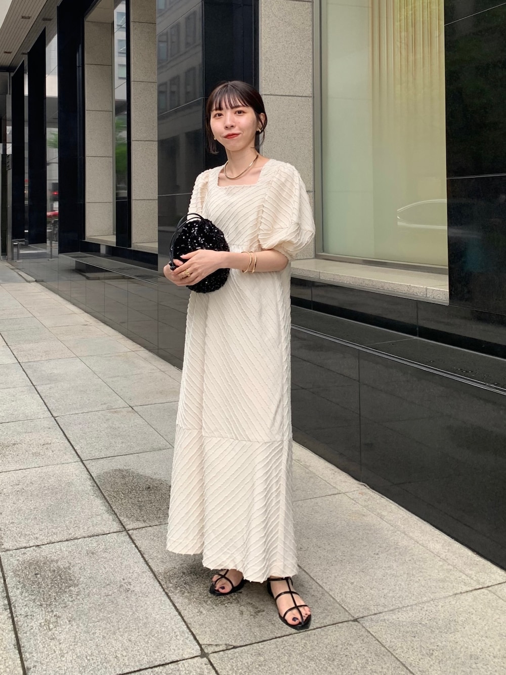 ホワイト系のワンピース、ブラック系のハンドバッグ、ブラック系のサンダルを着用したレディースの春コーディネートの1枚目の写真