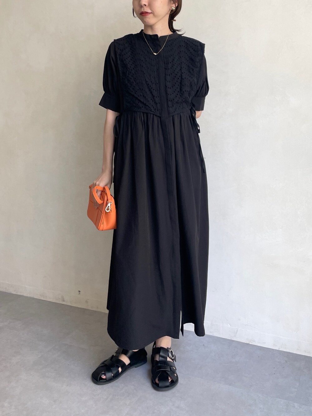 ブラック系のワンピース、オレンジ系のショルダーバッグ、ブラック系のサンダルを着用したレディースの夏コーディネートの2枚目の写真