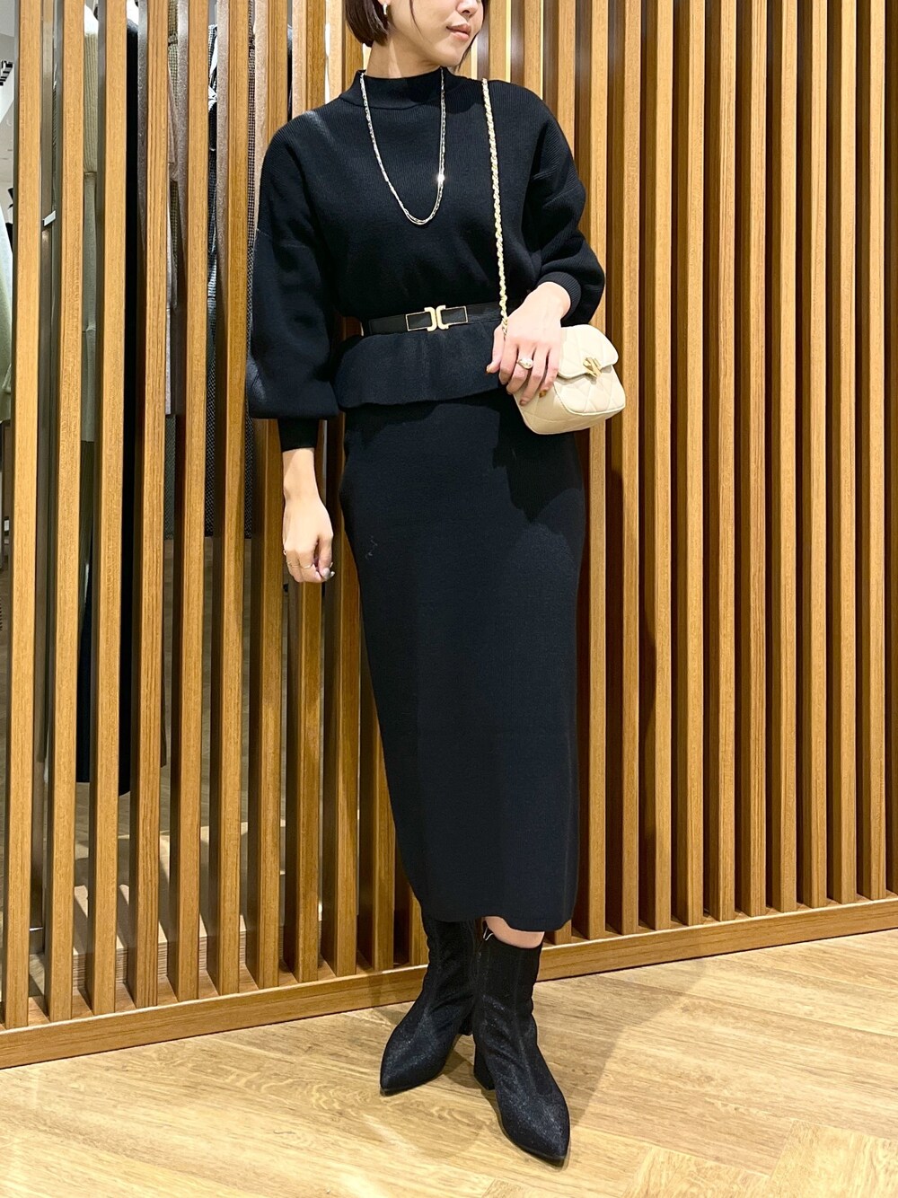 ブラック系のワンピース、ベージュ系のショルダーバッグ、ブラック系のブーツを着用したレディースの秋コーディネートの1枚目の写真