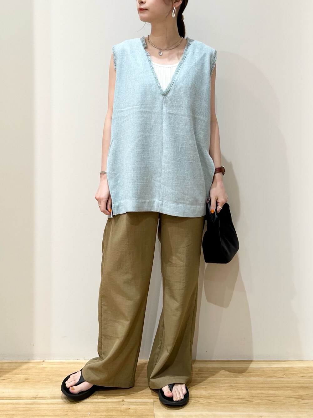 グリーン系のベスト、ブラック系のハンドバッグ、ブラック系のサンダルを着用したレディースの夏コーディネートの1枚目の写真