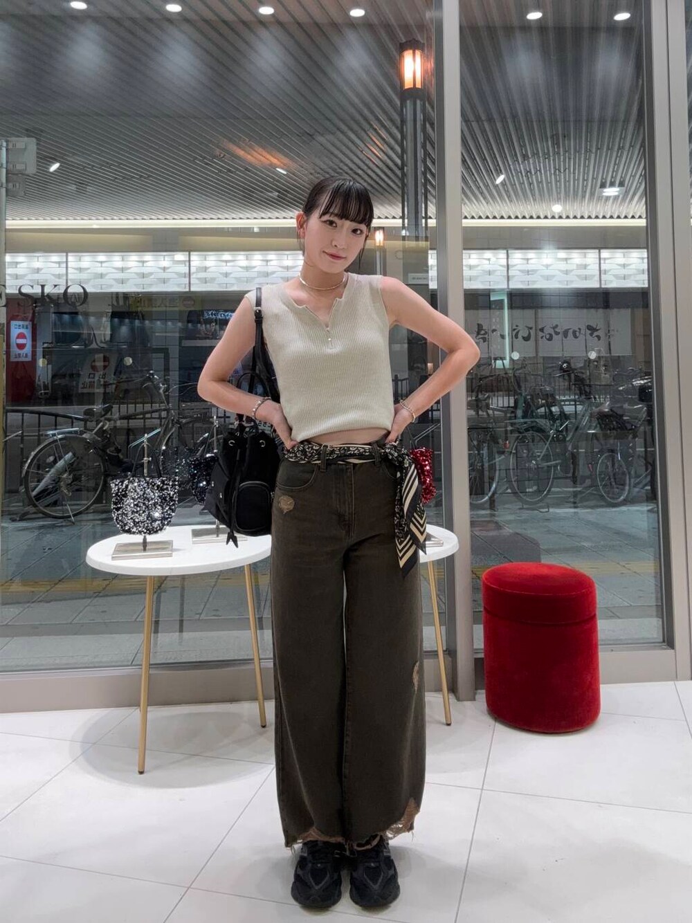ブラック系のショルダーバッグ、ベージュ系のニット/セーター、ブラウン系のデニムパンツを着用したレディースの夏コーディネートの1枚目の写真