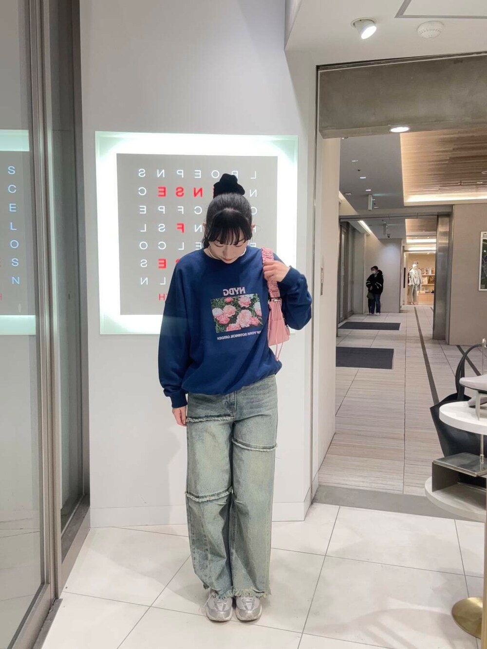 レッド系のショルダーバッグ、ブルー系のデニムパンツ、ブルー系のスウェットを着用したレディースの春コーディネートの1枚目の写真
