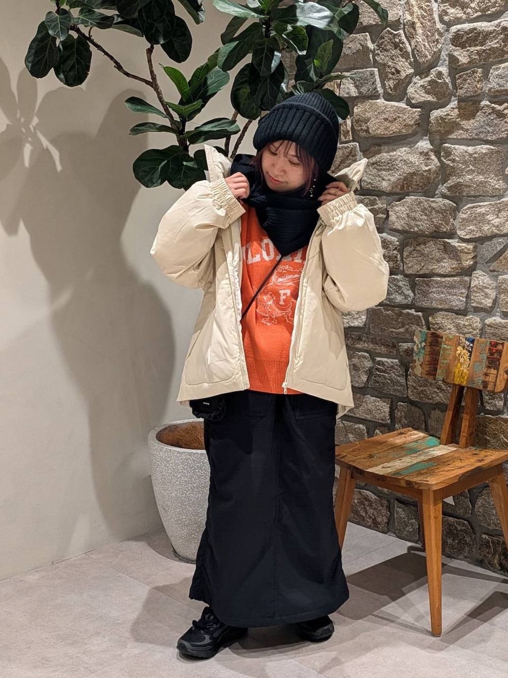 ブラック系のスカート、オレンジ系のニット/セーター、ホワイト系のダウンジャケット/コートを着用したレディースの冬コーディネートの1枚目の写真