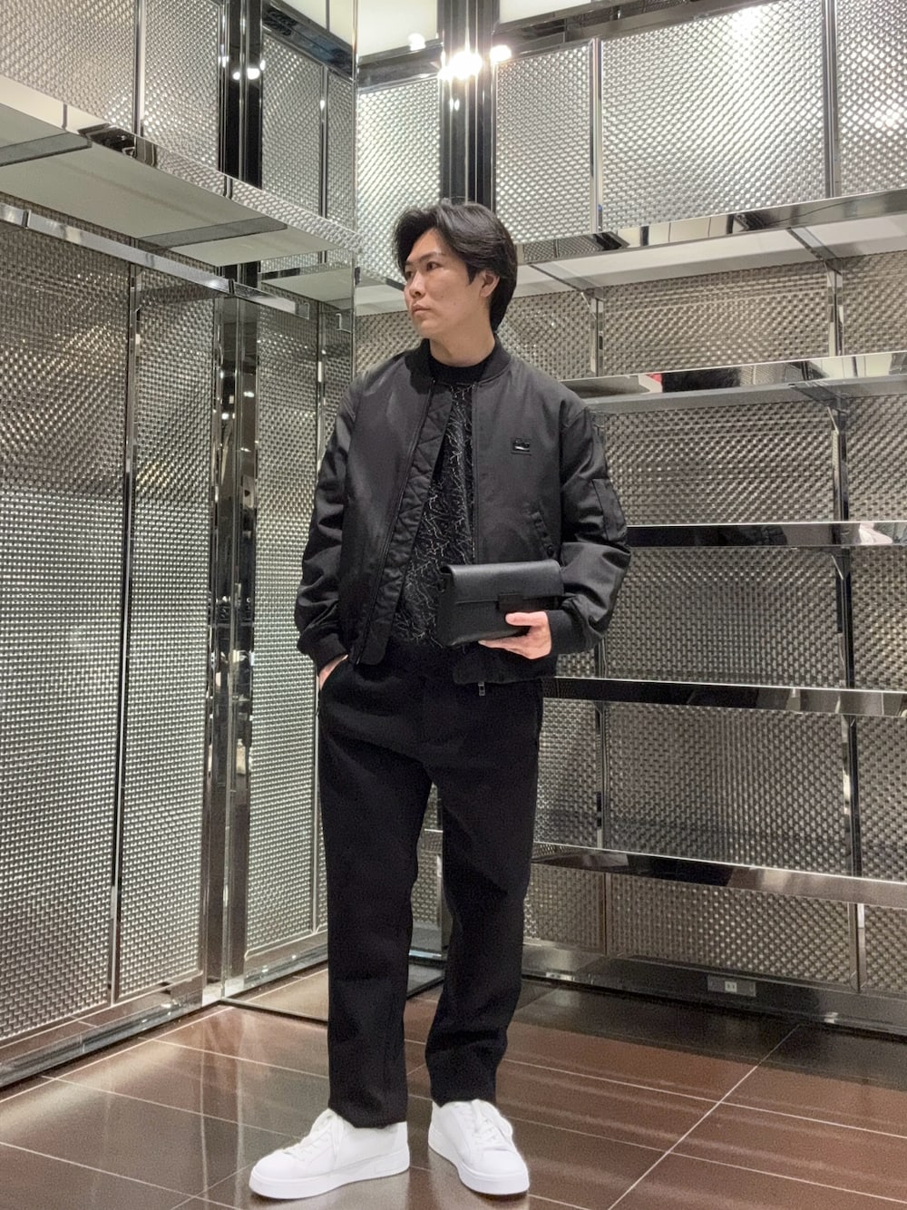 ブラック系のショルダーバッグ、ブラック系のスラックス、ホワイト系のスニーカーを着用したメンズの秋コーディネートの1枚目の写真