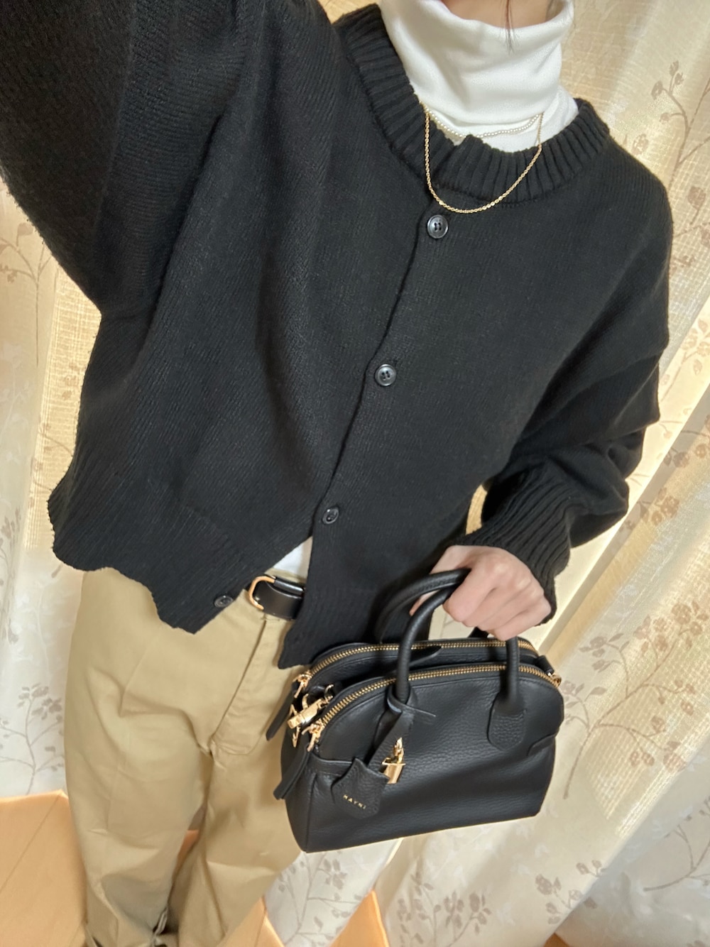 ベージュ系のチノパンツ、ブラック系のショルダーバッグ、ブラック系のカーディガン/ボレロを着用したレディースの秋コーディネートの1枚目の写真