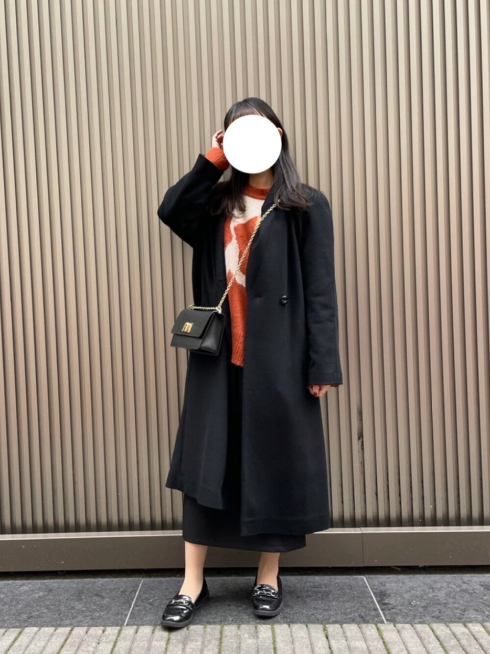 オレンジ系のニット/セーター、ブラック系のショルダーバッグ、ブラック系のスカートを着用したレディースの冬コーディネートの1枚目の写真
