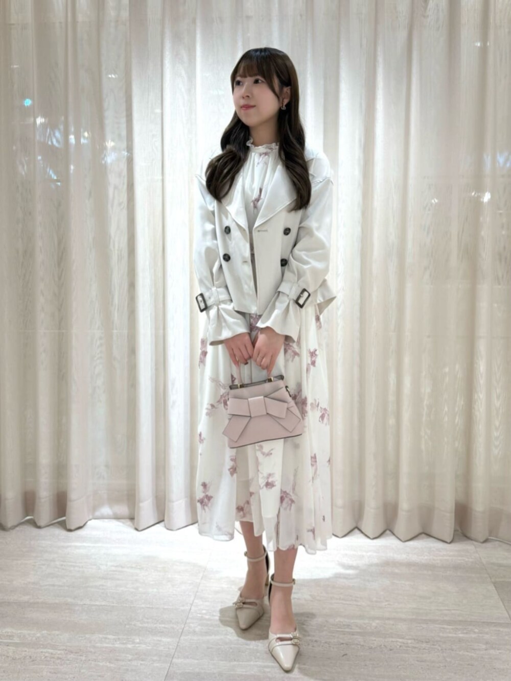 ベージュ系のパンプス、ピンク系のショルダーバッグ、ホワイト系のトレンチコートを着用したレディースの冬コーディネートの1枚目の写真