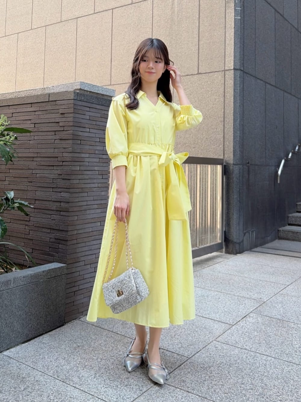 ブラック系のショルダーバッグ、イエロー系のワンピース、シルバー系のパンプスを着用したレディースの春コーディネートの1枚目の写真