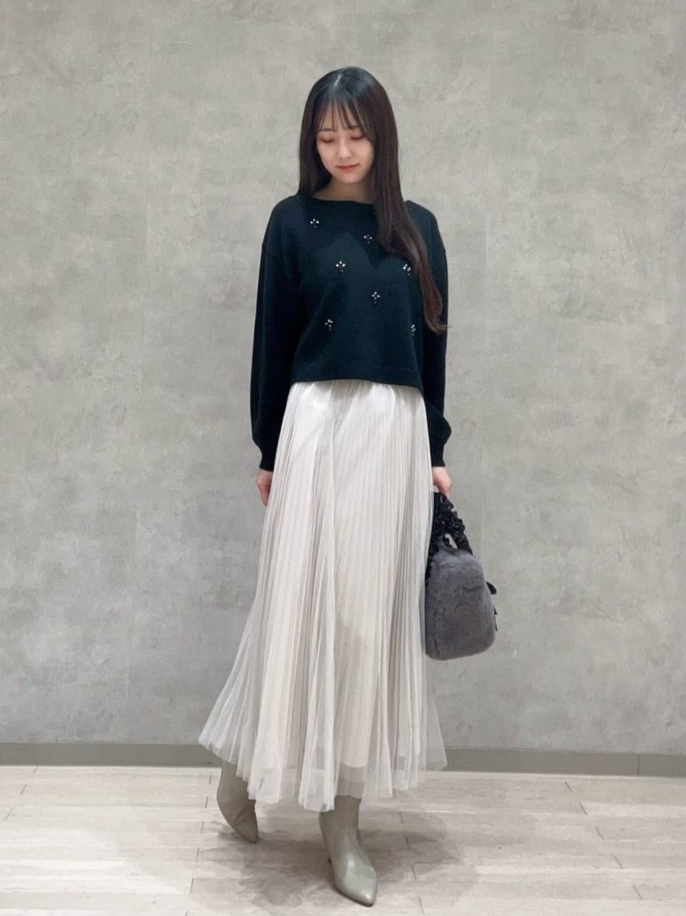 グレー系のトートバッグ、ブラック系のニット/セーター、ホワイト系のスカートを着用したレディースの冬コーディネートの1枚目の写真