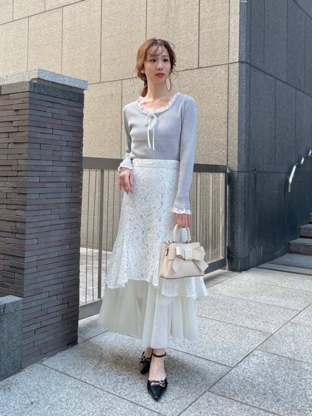 ホワイト系のショルダーバッグ、ブラック系のパンプス、グレー系のニット/セーターを着用したレディースの春コーディネートの1枚目の写真