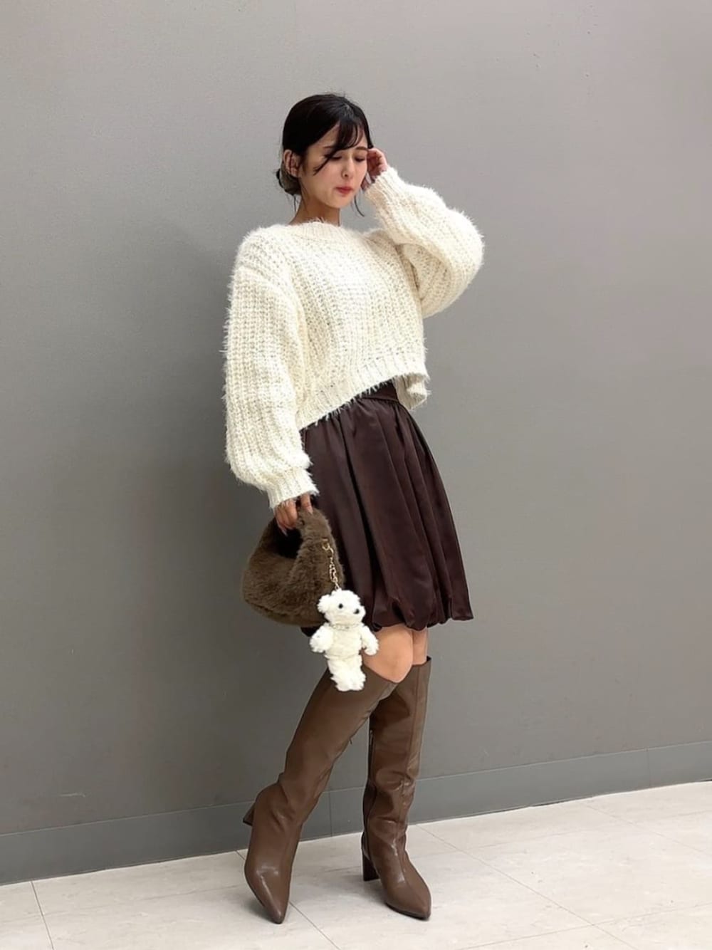 ブラウン系のブーツ、ブラウン系のハンドバッグ、ホワイト系のニット/セーターを着用したレディースの秋コーディネートの1枚目の写真