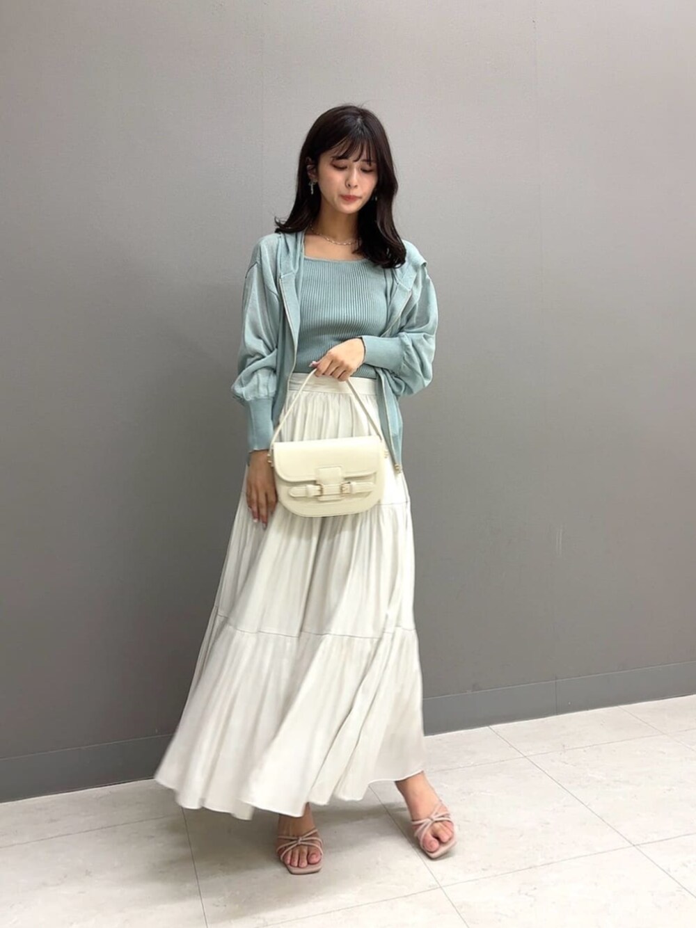 ホワイト系のショルダーバッグ、ホワイト系のスカート、グリーン系のパーカーを着用したレディースの夏コーディネートの1枚目の写真